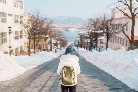 Foto de Mujer turista Visitando en Hakodate, viajero en suéter visitando la ladera de Hachiman Zaka con nieve en invierno. hito y popular para las atracciones en Hokkaido, Japón. Concepto de viajes y vacaciones - Imagen libre de derechos