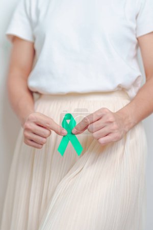 Photo for Woman holding Teal Ribbon on abdomen for January Cervical Cancer Awareness month. Uterus and Ovaries, Cervix, Endometriosis, Hysterectomy, Uterine fibroids, Reproductive and World cancer day concept - Royalty Free Image