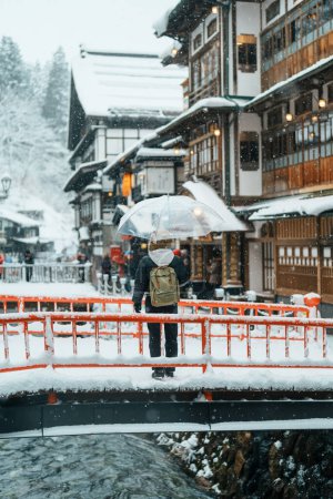 Téléchargez les photos : Femme touriste Visiter Ginzan Onsen à Yamagata, heureux Voyageur visiter le village japonais Onsen avec de la neige en saison hivernale. repère et populaire pour l'attraction au Japon. Voyage et vacances concept - en image libre de droit