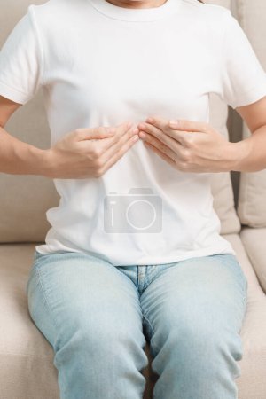 Photo for Woman having abdomen ache due to Stomach pain, digestion with constipation or Diarrhea from food poisoning and liver cancer on the sofa at home - Royalty Free Image