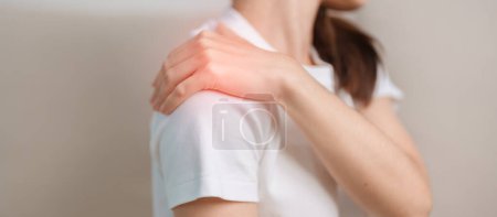 Téléchargez les photos : Femme souffrant de douleurs à l'épaule et au cou pendant qu'elle était assise sur le canapé à la maison. Douleurs musculaires dues au syndrome de douleur myofasciale et à la fibromyalgie, rhumatisme, douleur scapulaire, colonne cervicale. concept ergonomique - en image libre de droit