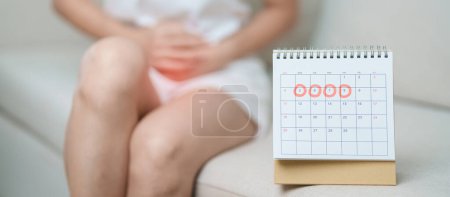 Photo for Menstruation period cycle of monthly and Stomachache concepts. woman having abdomen pain with calendar, illness female suffer from premenstrual ache and body Health problem on sofa at home - Royalty Free Image