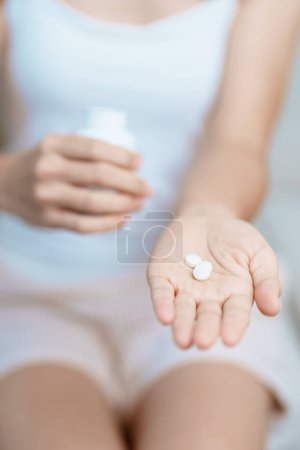 Frau hält Medikament Schmerztablette auf dem Sofa zu Hause, Einnahme gegen Kopfschmerzen, Magenschmerzen, Durchfall Schmerzen durch Lebensmittelvergiftung, Endometriose, Hysterektomie und Menstruation