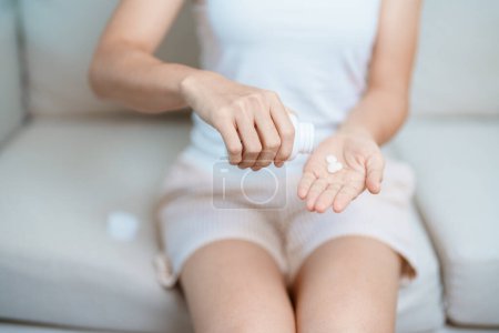 Frau hält Medikament Schmerztablette auf dem Sofa zu Hause, Einnahme gegen Kopfschmerzen, Magenschmerzen, Durchfall Schmerzen durch Lebensmittelvergiftung, Endometriose, Hysterektomie und Menstruation