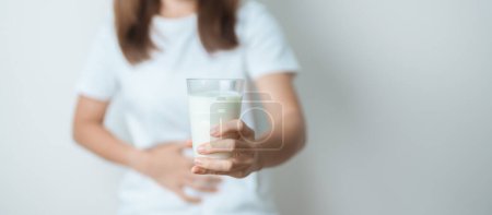 Intolérance au lactose et concept d'allergie au lait. femme tenir verre de lait et avoir des crampes abdominales et de la douleur quand boire du lait de vache. Symptômes maux d'estomac, intolérance aux produits laitiers, nausées, ballonnements, gaz et diarrhée