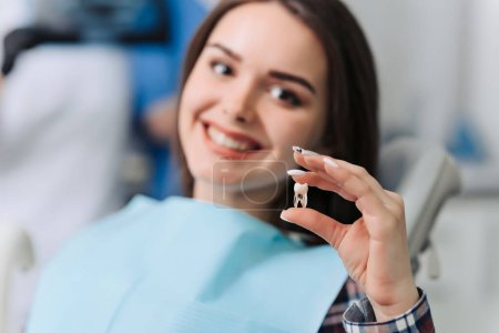Photo for Female patient shows false tooth in her hands in dentist office. - Royalty Free Image