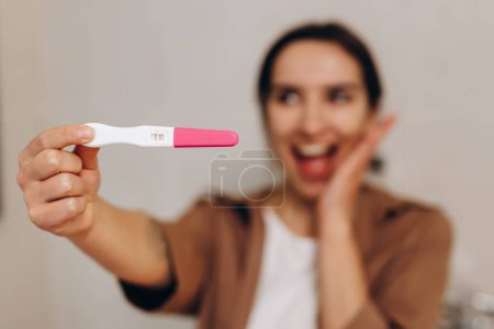 Foto de Happy young girl holding a positive pregnancy test in her hands. She is incredibly happy about this news. Happy motherhood and pregnancy concept. - Imagen libre de derechos