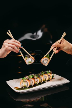 Téléchargez les photos : Sushi Chuka Roll et baguettes chinoises dans les mains sur le plat sur la table sur le fond flou - en image libre de droit