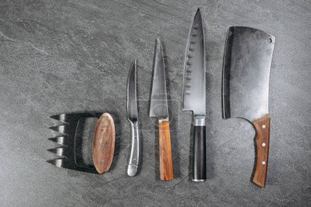 Ein Satz professioneller Küchenmesser bestehend aus einem Fünf-Klingen-Messer, einem kleinen Rundmesser, einem scharfen, geraden Messer, einem großen scharfen Entsteinungsmesser und einem Beilmesser auf einem steinernen Küchentisch