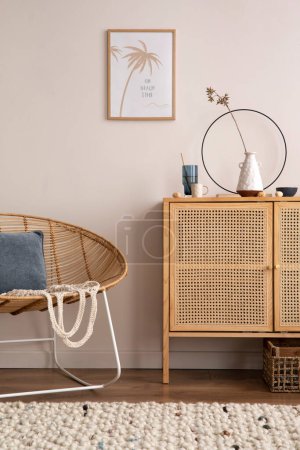 Photo for Cozy composition of living room interior with mock up poster frame, rattan comode, stylish armchair,  blue pillow, vase with dried flwers, beige wall, armchair and personal accessories. Home decor. Template. - Royalty Free Image