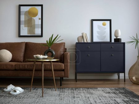Foto de Interior design of harmonized living room with mock up poster frame, brown sofa, navy commode, coffee table, carpet, leaf in vase, and personal accessories. Creative home decor. Template. - Imagen libre de derechos