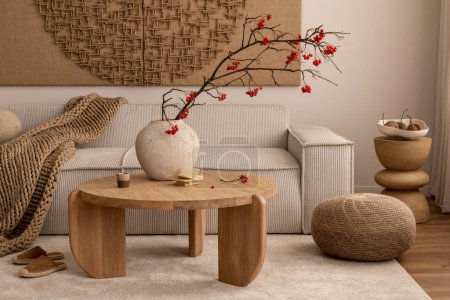 Creative composition of living room interior with wall art paint, modern beige sofa, round wooden coffee table, vase with rowan, brown pouf, slippers and personal accessories. Home decor. Template.