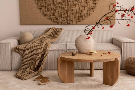 Warm and cozy living room interior with mock up poster frame, modular beige sofa with pillows, round coffee table, vase with rowan, rug, slippers and personal accessories. Home decor. Template.