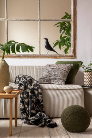 Téléchargez les photos : Warm and cozy living room interior with beige modular sofa, big window, patterned pillows, braided plaid, black bird, vase with leaves, plants,  and personal accessories. Home decor. Template. - en image libre de droit