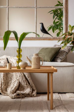 Téléchargez les photos : Aesthetics composition of open space interior with modular sofa, wooden coffee table, beige pitcher, window, braided plaid, glass vase with leaves and personal accessories. Home decor. Template. - en image libre de droit