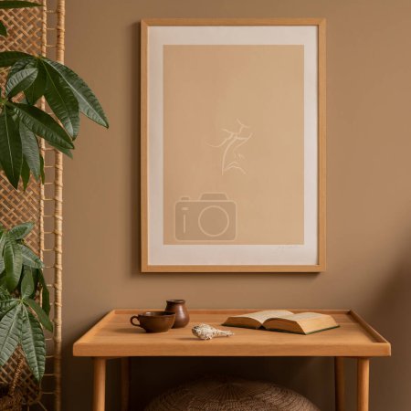 Composition chaleureuse et confortable de l'intérieur du salon avec un cadre d'affiche maquillé, une table en bois simple, un fauteuil en rotin, un mur de séparation, des plantes, un livre et des accessoires personnels. Décor intérieur. Modèle de modèle.
