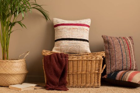 Photo for Minimalist composition of living room with colorful pillows, stylish wicker basket, claret plaid, beige wall, plants in basket, book, brown wall and personal accessories. Home decor. Template. - Royalty Free Image
