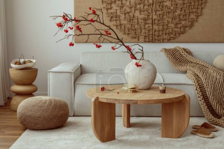 Photo for Creative composition of living room interior with wall art paint, modern beige sofa, round wooden coffee table, vase with rowan, brown pouf, slippers and personal accessories. Home decor. Template. - Royalty Free Image
