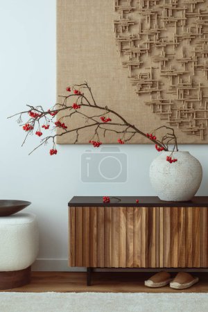 Photo for Minimalist composition of living room interior with mock up poster frame, vase with rowan, wooden sideboard, carpet, slippers, white pouf and personal accessories. Home decor. Template. - Royalty Free Image