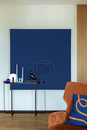 Minimalist composition of living room interior with mock up poster frame, orange armchair, blue pillow, black consola, candles, bird sculpture and personal accessories. Home decor. Template.