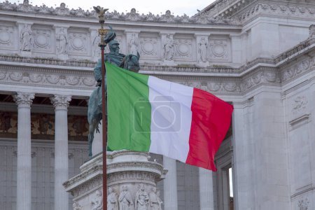 Italian flag against the background of the Vittoriano monument with a gigantic equestrian statue of King Vittorio Emanuele II in Rome, Italy
