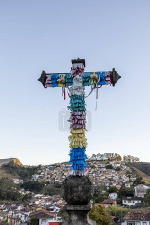 Photo for Cross decorated with ribbons for June festivals with the city on background. Ouro Preto, State of Minas Gerais, Brazil - Royalty Free Image