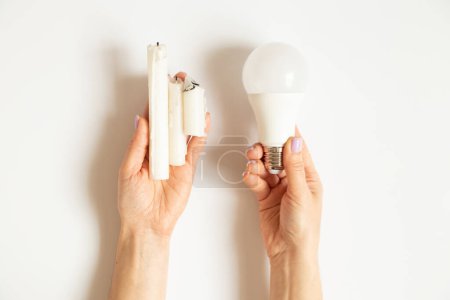 Foto de Bombilla led y velas en las manos de una chica sobre un fondo blanco, electricidad y opciones de ahorro, sin luz - Imagen libre de derechos