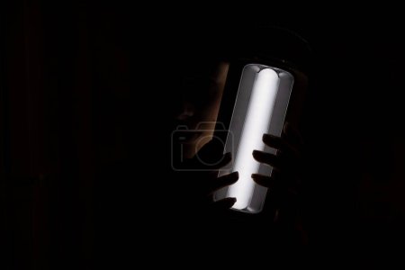 Foto de Chica ucraniana con una linterna led en una batería en la oscuridad en casa sin luz después de los ataques con cohetes en Ucrania sin luz, la guerra en Ucrania, Ucrania sin luz - Imagen libre de derechos