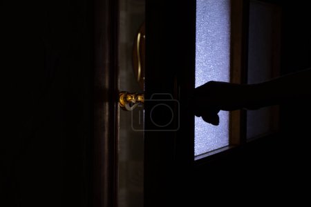 Foto de La mano de mujer abre la puerta en la oscuridad en casa, pomo de la puerta - Imagen libre de derechos