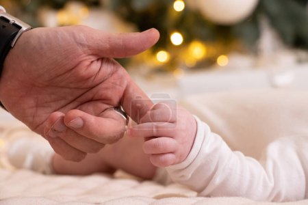 Photo for Dad's hand holds the hand of a newborn under the New Year tree, love, the hand of a newborn - Royalty Free Image