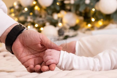 Photo for Dad's hand holds the hand of a newborn under the New Year tree, love, the hand of a newborn - Royalty Free Image