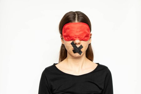 Téléchargez les photos : A girl with a blindfold and a closed mouth with a band-aid on an isolated background, a blind and dumb girl - en image libre de droit