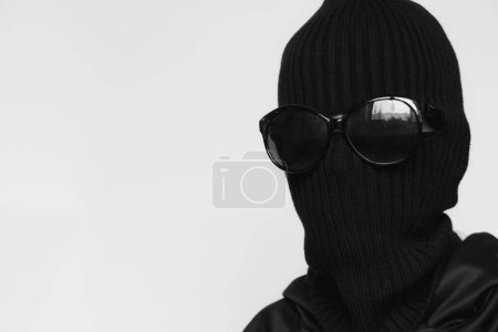 Foto de Sombrero de pasamontañas sobre una chica y gafas de sol sobre un fondo blanco, la cara de un ladrón en un sombrero con una ranura para verbos - Imagen libre de derechos