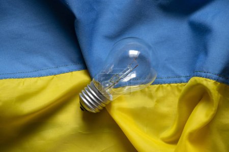 Foto de An incandescent lamp lies on the flags of Ukraine, people without light in Ukraine due to Russian missile attacks, war, crisis - Imagen libre de derechos