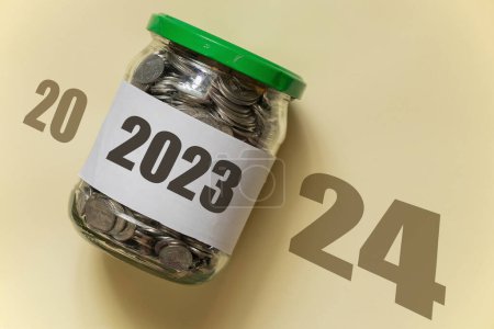 2023 is written on a bank of pennies which lies on a brown background with the text 2024, business in the new year and income, profit