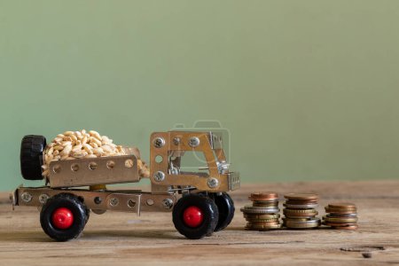 Photo for Cargo transportation of grain on a children's typewriter from a metal constructor on a wooden board and stacks of coins stand side by side, logistics and finance, grain transportation and business - Royalty Free Image