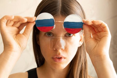 Téléchargez les photos : Drapeau de la Russie sur les lunettes d'une fille, aveugle et trompé par la propagande russe, ne voit rien à cause de la propagande - en image libre de droit