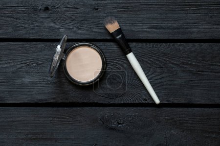Photo for Face foundation in plastic and a powder brush lie on a black wooden board, cosmetics and fashion - Royalty Free Image