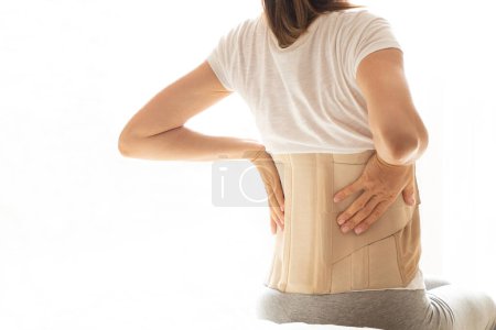 Frau mit einem Korsett auf dem Rücken, um ihren Rücken vor Schmerzen in Rücken und Wirbelsäule zu stützen, medizinisches Konzept, Rückenstütze, Rückenschmerzen, Tragen einer Spange zu Hause