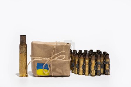 Photo for An automatic rifle casing and a ribbon with bullet casings stand next to a box on which the flag of Ukraine is painted, humanitarian aid in the form of weapons for Ukraine, war - Royalty Free Image