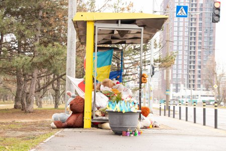 Dnipro, Ukraine, Blumen, Kinderspielzeug, Kerzen, ein Erinnerungsort in der Nähe eines Wohnhauses an einer Bushaltestelle, zerstört durch eine russische Rakete, die Flagge Japans und der Ukraine
