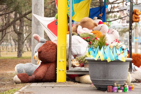 Dnipro, Ukraine, Blumen, Kinderspielzeug, Kerzen, ein Erinnerungsort in der Nähe eines Wohnhauses an einer Bushaltestelle, zerstört durch eine russische Rakete, die Flagge Japans und der Ukraine