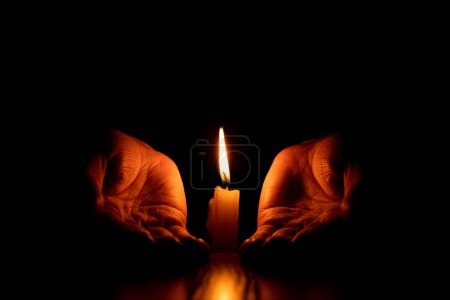 Frauenhände neben einer Kerzenflamme im Dunkeln, Glaube und Religion im Gebet