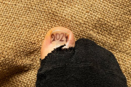 2024 is drawn on a girls toe that sticks out of a torn sock, poverty and failure