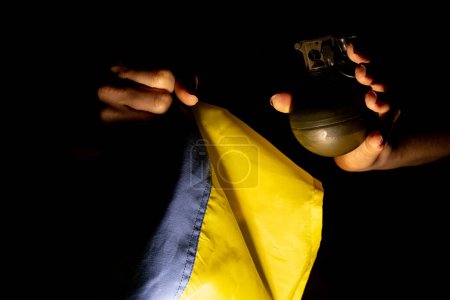 Foto de Una granada de mano en las manos de una niña en la oscuridad y la bandera de Ucrania, una granada de combate, ayuda para Ucrania - Imagen libre de derechos
