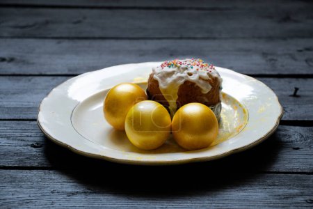 Homemade Easter cake and golden colored eggs stand on a plate on a black board, Easter holiday in Ukraine