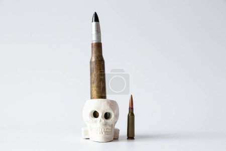 Two bullets, large and small, and a plaster skull on a white background