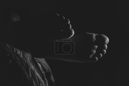 A man's legs on the bed when he lies in the dark black and white photo, men's feet