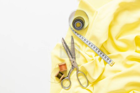 Spools of thread, measuring tape, sewing scissors and yellow fabric on a white background, sewing