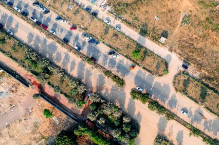 Téléchargez les photos : Drone aérien vue de haut en bas de la route rurale en Inde avec des feilds stériles poussiéreux des deux côtés et des ombres d'arbres avec des voitures garées en Inde - en image libre de droit